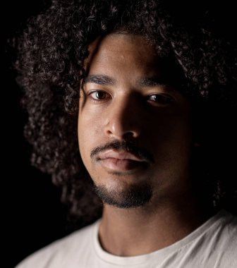 Stüdyoda siyah arka planda poz veren kıvırcık saçlı ve keçi sakallı Afro-Amerikan bir adamın portresini yakından çek.