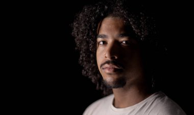 Siyah arka planda kıvırcık saçlı, kendinden emin Afro-Amerikan bir adamın stüdyo portresi.