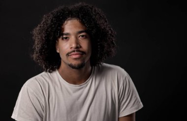 Siyah arka planda güvenle poz veren kıvırcık saçlı genç Afrikalı Amerikalı adam.