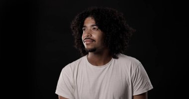 Siyah arka planda gülümseyen kıvırcık saçlı Afro-Amerikan bir adamın portresi.