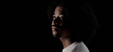 Umut dolu Afrikalı Amerikalı genç adam siyah arka planda izole bir şekilde yukarı bakıyor.