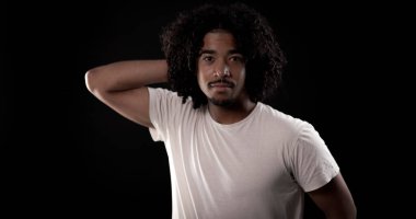 Beyaz tişörtlü, siyah arka planda poz veren Afro-Amerikan bir adamın stüdyo portresi.