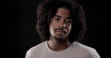 Siyah arka planda poz veren kıvırcık saçlı ve keçi sakallı genç Afrikalı Amerikalı adam.