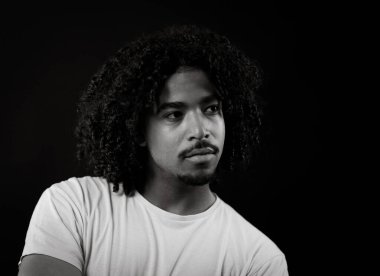 Siyah beyaz, kıvırcık saçlı genç bir Afrikalı Amerikalı 'nın portresi. Kameradan karanlık bir arka plana bakıyor.