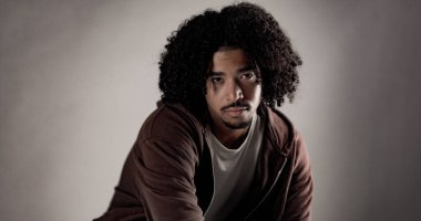 Kıvırcık saçlı, keçi sakallı, gri arka planlı stüdyoda poz veren ciddi bir Afro-Amerikan 'ın portresi.