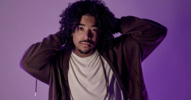 Mor stüdyo ışıklarıyla aydınlatılmış, elleriyle başını tutan şık genç bir adam.