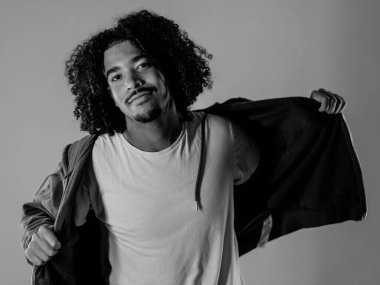 Genç adam siyah beyaz keçi sakalı ve kıvırcık saçlarıyla kazağını açıyor.