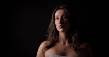 Siyah arka planda dudaklarını büzen genç bir kadının stüdyo portresi.