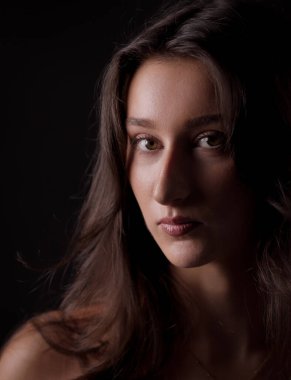 Uzun kahverengi saçlı güzel bir kadının stüdyo portresi siyah arka plana karşı ciddi bir ifade sergiliyor.