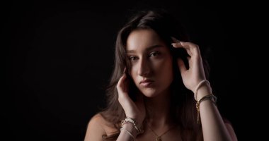 Siyah arka planda poz veren güzel bir modelin stüdyo portresi, saçına dokunuyor.