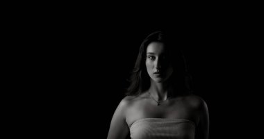 Yüzünün yarısı aydınlanmış, gizemli ve entrika dolu genç bir kadının dramatik siyah beyaz portresi.