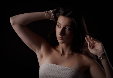 Siyah bir arka planda el ve saçla poz veren genç bir kadının stüdyo portresi.