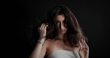 Uzun kahverengi saçlarıyla oynayan genç bir kadının stüdyo portresi