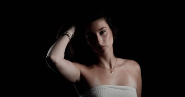 Siyah arka planda saçını tutan genç bir kadının stüdyo portresi.