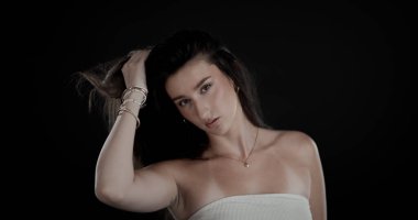 Kolye ve bilezik takan, elleri saçı olan genç bir kadının stüdyo portresi.