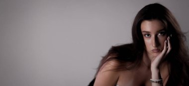 Stüdyo portresi. Uzun kahverengi saçlı, elinde dinlenen genç bir kadın.