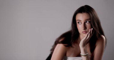 Uzun kahverengi saçlı, eli çenesinde düşünceli genç bir kadın.