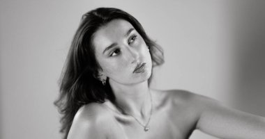 Moda fotoğrafçılığı için poz veren kahverengi saçlı ve çıplak omuzlu güzel bir genç kadının stüdyo portresi.