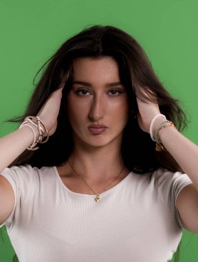 Beyaz tişört ve bilezik giyen genç bir kadın yeşil ekranda saçına dokunuyor.