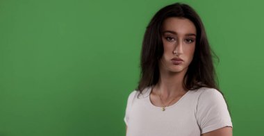 Uzun kahverengi saçlı, yeşil ekran arka planında poz veren ciddi bir genç kadının stüdyo fotoğrafı.