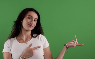 Yeşil ekran arkaplanını gösteren ve işaret eden genç bir kadın