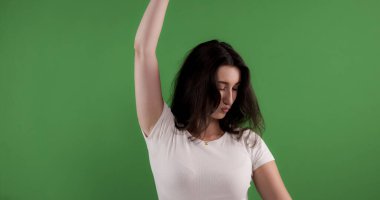 Beyaz tişört giyen genç bir kadın. Krom anahtar yeşil arka planda kolunu kaldırıyor.