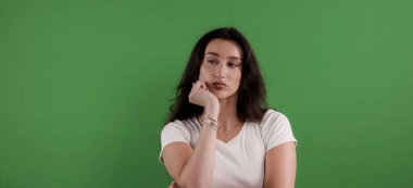 Elleri çenesinde, yeşil ekran krom anahtar arka planına bakan sıkılmış genç bir kadın.