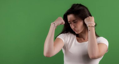 Genç bir kadın kaslarını esnetiyor ve gücünü yeşil bir ekranda gösteriyor.