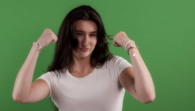 Genç bir kadın yeşil arka planda kaslarını ve gücünü gösteriyor.