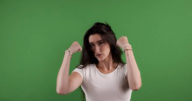 Güçlü genç bir kadın yeşil ekran arka planında kaslarını esnetiyor. Güç ve kararlılık gösteriyor.