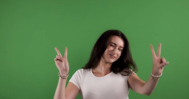 İki eliyle barış işareti yapan genç bir kadın, krom anahtar arka planda göz kırpıyor ve gülümsüyor.