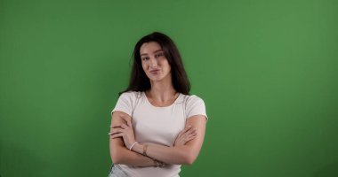 Genç bir kadın yeşil ekranda kendine güvenen bir ifadeyle kollarını kavuşturuyor.