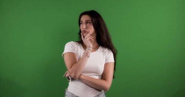 Düşünceli genç bir kadın, eli çenesinde. Krom anahtar arka planına bakıyor.