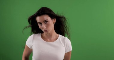 Yeşil ekran arka planında saç üfleyen genç bir kadının stüdyo fotoğrafı.