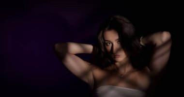 Kolları havada genç bir kadının stüdyo portresi. Yüzüne ve vücuduna mor bir arka plana çizgili gölgeler çiziyor.