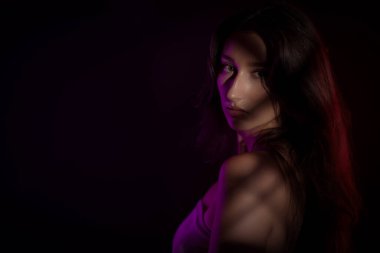 Uzun kahverengi saçlı, pembe ve mor neon ışıklarla aydınlatılmış, sanatsal ve anımsatıcı bir atmosfer yaratan genç bir kadının stüdyo portresi.