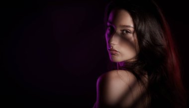 Stüdyo portresi, uzun saçlı, yüzü ve omzunda gölgelerle poz veren genç bir kadın.