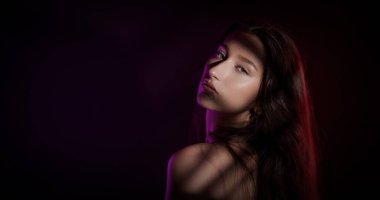 Yüzünde ve vücudunda gölgeler olan, renkli ışıklar altında poz veren güzel bir kadının stüdyo portresi.