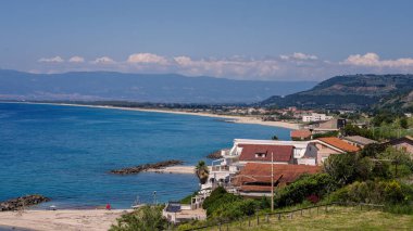 Güney İtalya, Calabria 'da mavi gökyüzü altında evler, sahil, turkuaz su ve dağların bulunduğu Tropea kıyı şeridinin manzarası