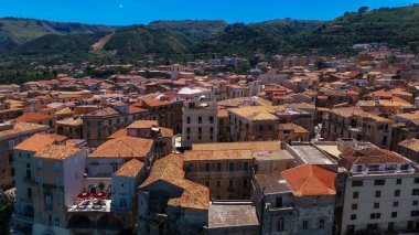 İtalya 'nın Calabria kentindeki Tropea şehrinde yoğun bir şekilde doldurulmuş kırmızı kiremit çatılı, canlı mavi gökyüzü altında geleneksel binalar bulunmaktadır.