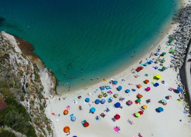 Tropea, Calabria, İtalya 'da turkuaz Akdeniz' de yüzen renkli plaj şemsiyeleri ve turistlerin hava manzarası
