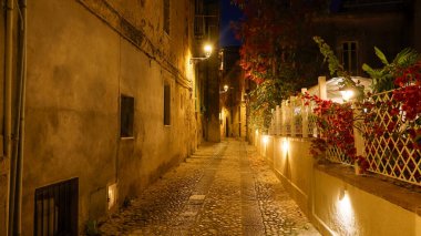 Gece Tropea, İtalya 'da dar bir kaldırım taşından geçidi aydınlatan sıcak ışıklar sağda bir restoran var.