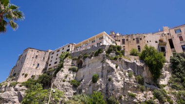Tropea, Calabria, Güney İtalya 'da açık mavi bir gökyüzünün altında denize bakan bir uçurumun üzerinde duran beyaz ve sarı binalar.