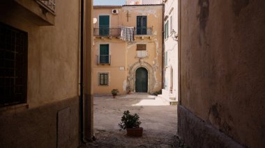 Tropea 'nın tarihsel cazibesini yakalayan yıpranmış binalar ve saksı bitkileriyle ıssız bir avluya açılan dar bir sokak.