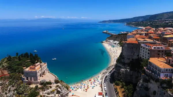 Turkuaz Tyrhenian Denizi, kumlu plaj, renkli şemsiyeler ve Santa Maria dell 'Isola Sığınağı ile Tropea, Calabria' nın havadan görünüşü