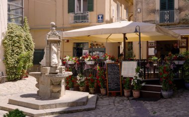 TROPEA, ITALY - HAZİRAN 02, 2025 - İtalya 'nın Tropea kentindeki bir meydandaki geleneksel bir taş çeşmenin fıskiyesi, bir restoranı ve arka plandaki açık oturma alanı