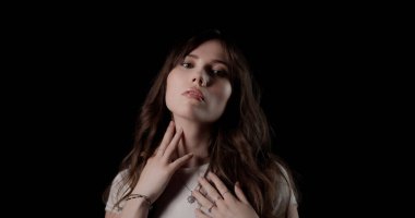 Genç bir kadının stüdyo portresi nazikçe boynuna ve göğsüne dokunuyor.