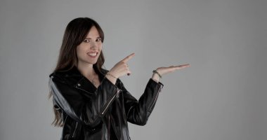 Gülümseyen sanatçı işaret parmağıyla işaret ediyor ve avuç içini gri arka planda açıyor.