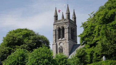 Azizler Kilisesi 'nin saat ve bayrağı Helmsley, İngiltere' de yemyeşil ağaçlarla çevrili taş kulesi.