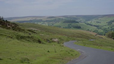 Kuzey York Moors Ulusal Parkı 'nın kıvrımlı yeşil tepelerinin ortasındaki dolambaçlı bir yolun manzarası İngiliz kırsalının güzelliğini gözler önüne seriyor.